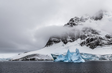 Huge steep stone rock covered with glacier and drifting blue iceberg, close to Argentine islands, Antarctica