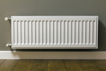 White heating radiator on wall in an apartment with wooden floor