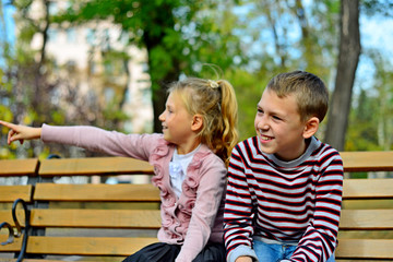 Obraz na płótnie Canvas Brother and sister cuddling and sitting on a bench in a park on autumn day. Little girl and boy hugging