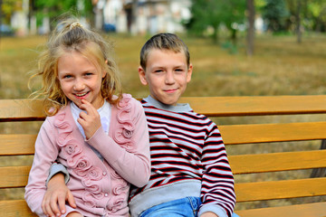 Fototapeta na wymiar Brother and sister cuddling and sitting on a bench in a park on autumn day. Little girl and boy hugging