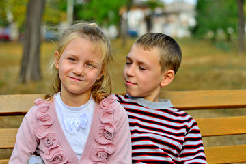 Fototapeta na wymiar Brother and sister cuddling and sitting on a bench in a park on autumn day. Little girl and boy hugging