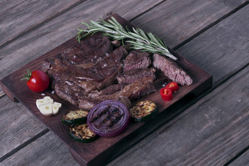 Grilled beef striploin steak and vegetables on wooden plate.