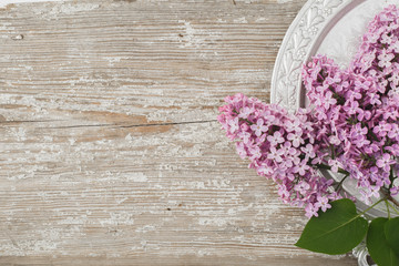 Beautiful lilac flowers lying on a silver saucer against the background of an old wooden plank with a texture paint