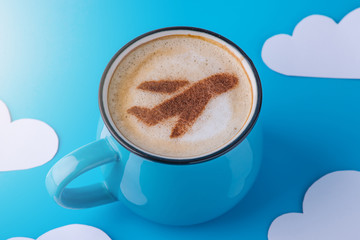 Cup of cappuccino with a picture of the plane on the foam. Blue sky background with paper clouds. Concept of travel