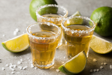 Macro focus photo of shots of golden Mexican tequila with lime and salt on wooden background....