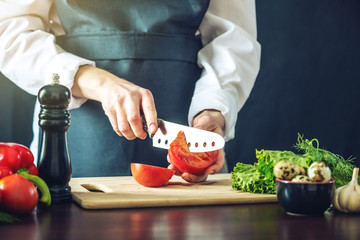 The chef in black apron cuts vegetables. Concept of eco-friendly products for cooking