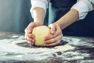 The chef in black apron makes pizza dough with your hands on the table