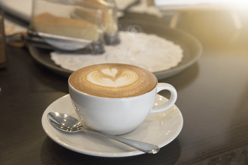 closeup hot coffee latte art cup with smoke on table.