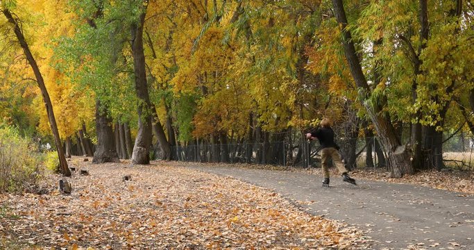Boy roller skates along beautiful autumn fall trail footpath.Season fall colors in forest along river bank. Golden yellow, golden, red and orange  leaves. Family exercise and outdoor fun.