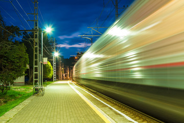 The illuminated platform of railway station and train in motion blur at twilight, Sochi, Russia