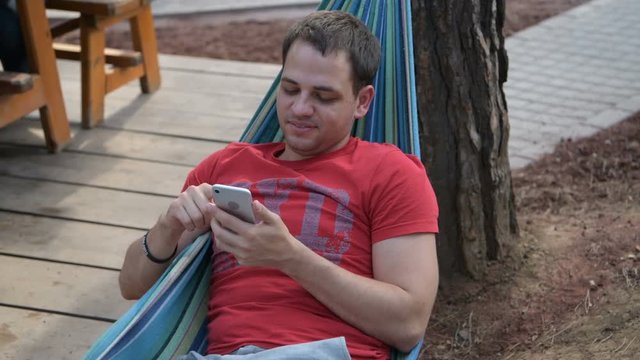 Man using mobile smart phone while relaxing in a hammock