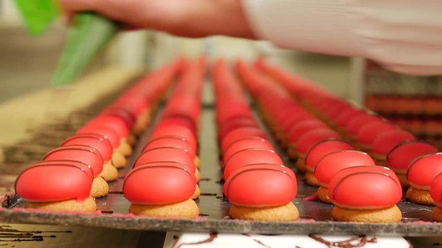 Red Petite fours pastry colorful sweet cakes being decorated with chocolate in a bakery factory
