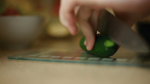 A young male guy slices a cucumber on a glass board. In the kitchen.