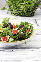 Autumn salad of arugula, figs in a white earthenware plate.