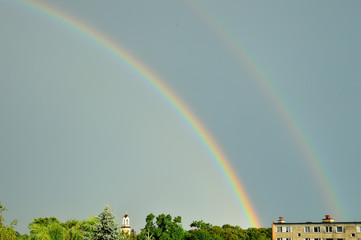 Tęcza na niebie po burzy nad dachami domów. © W Korczewski