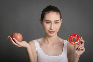 Beautiful Woman holding donuts and apple. Junk food, Slimming, weight loss.  People with sweets, dessert. Diet, dieting concept. Isolated on gray background