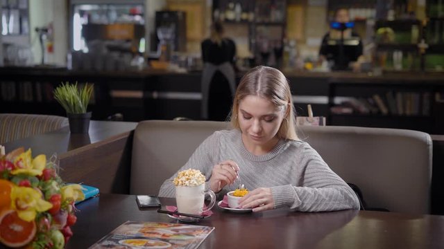 A young and pretty woman eating dessert and drinking milk frapes with caramel flavor, a lady loves to work herself with delicious dishes in a cafe