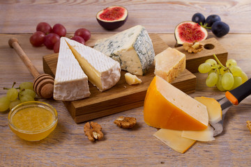 Cheese plate. Various types of cheese with grapes, honey, figs and nuts on rustic wooden table, horizontal