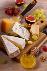 Cheese plate. Various types of cheese with grapes, honey, figs and nuts on rustic wooden table, vertical