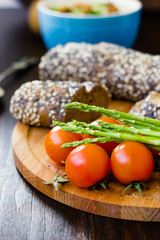 Fresh and ripe asparagus and cherry tomatoes with bread on wooden board.