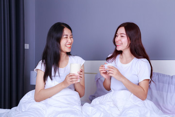 two best friends talking and drinking a cup of coffee on bed in bedroom