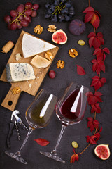 Red and white wine with cheese plate. Wine glasses with cheese,  grapes, figs and nuts on black background. Wine and food concept. View from above, top, vertical