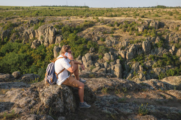 Young stylish man with a beard sitting on the precipice of the canyon on the phone