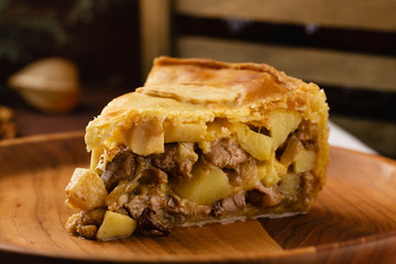 Piece of chicken meat pie with potatoes, apples and chanterelles on a wooden plate