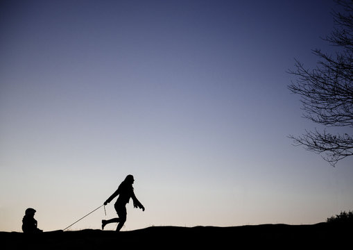Silhouette of a mother pulling her child in a sled across a field in winter