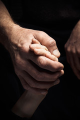 Hands of an elderly man holding the hand of a younger man.