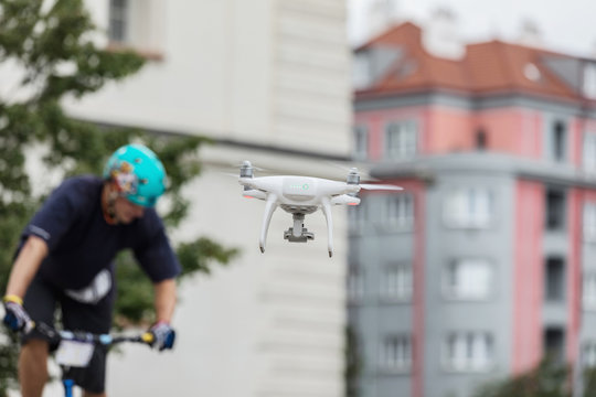 The White Dron shoots a biker in the city. Concept of sport, flying. Biker is out of focus, focus on the dron. White drone, quadrocopter, with photo camera flying in the city. Concept drone, sport.