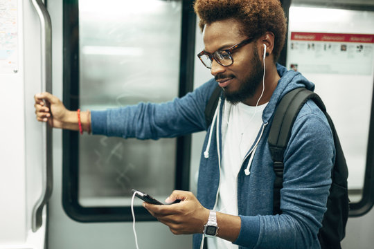 Young afro black man using mobile phone while listening music on the subway train.