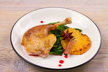 Duck leg with spinach and orange in sweet and sour berry sauce, white plate on rustic wooden table