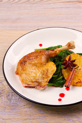 Duck leg with spinach and orange in sweet and sour berry sauce, white plate on rustic wooden table