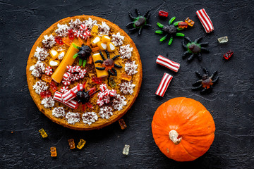 Halloween sweets. Pumpkin pie and gummy figures on black background top view