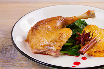 Duck leg with spinach and orange in sweet and sour berry sauce, white plate on rustic wooden table