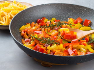 Cooking bell peppers with rosemary in skillet as sauce for italian pasta