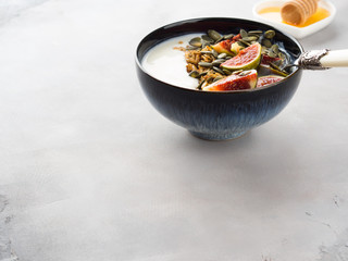Healthy breakfast natural yogurt bowl with home made granola, pumpkin seeds and figs on gray background