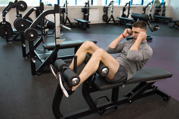 Fototapeta na wymiar Portrait of strong young man doing crunches on stand during work out in modern gym