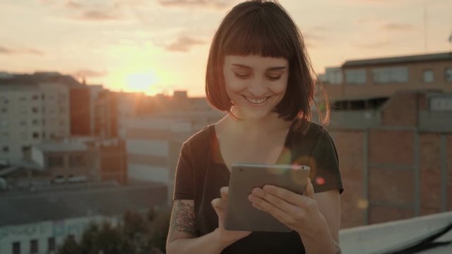 Attractive millennial young woman or happy pretty teenager stands in middle of busy buzzling city on summer sunset night. she uses mini tablet full of applications and technology