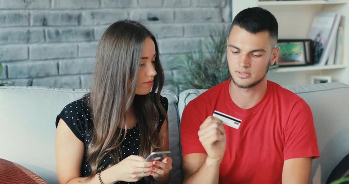Young couple at home buying on internet online shopping use phone communication credit card creditcard entertainment lifestyle love man woman payment Shot on RED EPIC camera. Slow Motion Shot.