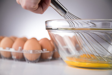 Hand rührt Eier für Rührei in Glas Schale mit Schneebesen