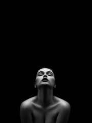 beautiful young naked woman posing sensually holding head up on black background with copy space, monochrome