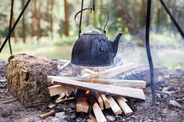 The teapot with tea is warmed up at the hearth in the woods