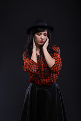 Emotion brunette female model posing in black hat with red bright lipstick on black background. Art fashion portrait.