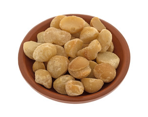 Dry roasted and salted macadamia nuts in a small terracotta bowl isolated on a white background.