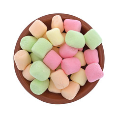 Top view of a small red clay bowl filled with colorful pastel hued miniature green, pink, yellow and orange marshmallows isolated on a white background.