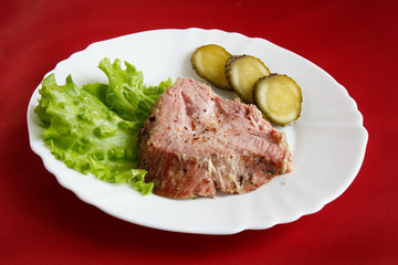 cut meat with slices of salted cucumber on white plate on the background of a red tablecloth