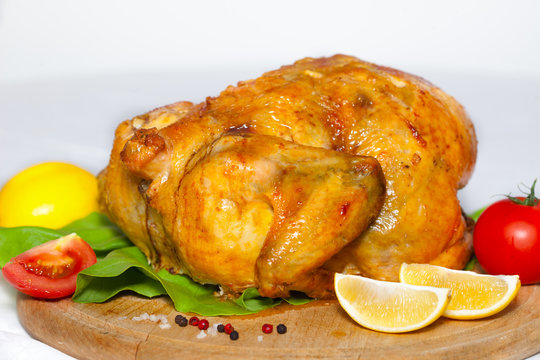 Roasted chicken with a golden crust with lemon and vegetables on a wooden board