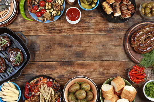 Outdoors Food Concept. Delicious Barbecued Steak, Sausages And Grilled Vegetables On A Wooden Picnic Table With Copy Space, Top View